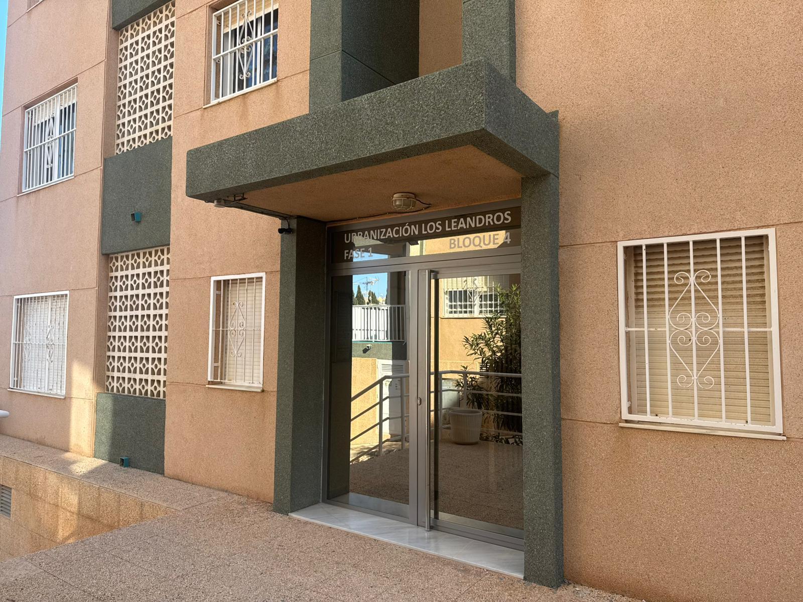 Entrance to a beige apartment building with glass double doors under a dark green granite canopy, barred windows nearby.