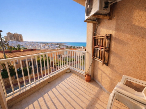 Sunlit balcony with a white railing overlooking a coastal town and the blue sea.