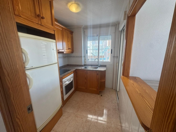 Cozy narrow kitchen with wooden cabinets, white fridge and stove, granite countertops, and a sink beneath a window.