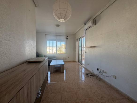 Living room with a wooden cabinet along the left wall, a light coffee table, and a gray sofa by a window with bars; balcony door on the right; tangled cables on the floor near outlets.