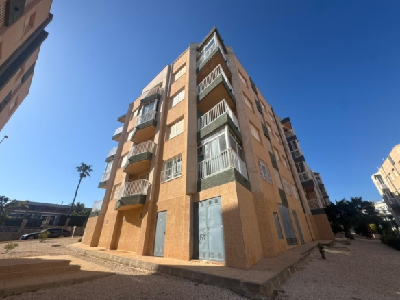 Tall peach-colored apartment building with white balconies under a clear blue sky, palm trees nearby.