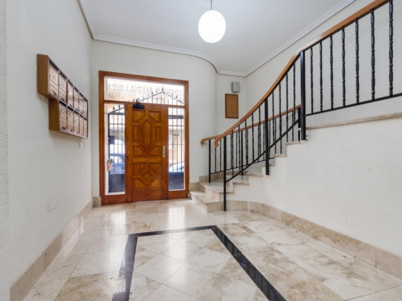Interior building lobby with a wooden front door, row of mailboxes on the left, and a curved staircase with black railings to the right.