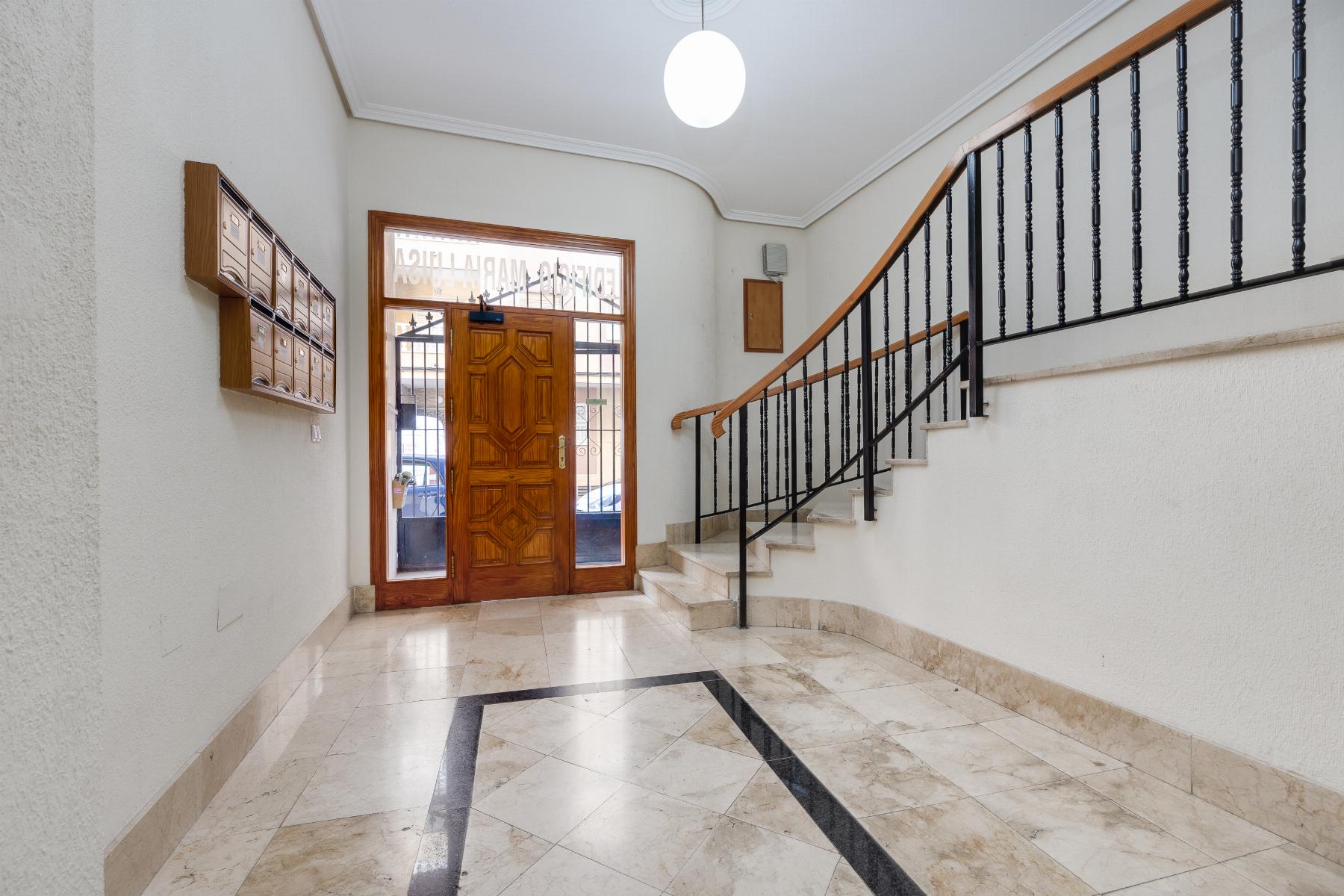 Interior building lobby with a wooden front door, row of mailboxes on the left, and a curved staircase with black railings to the right.