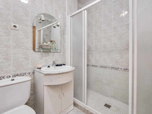 Small bathroom with a white vanity sink, oval mirror, and a glass‑door shower against tiled walls.