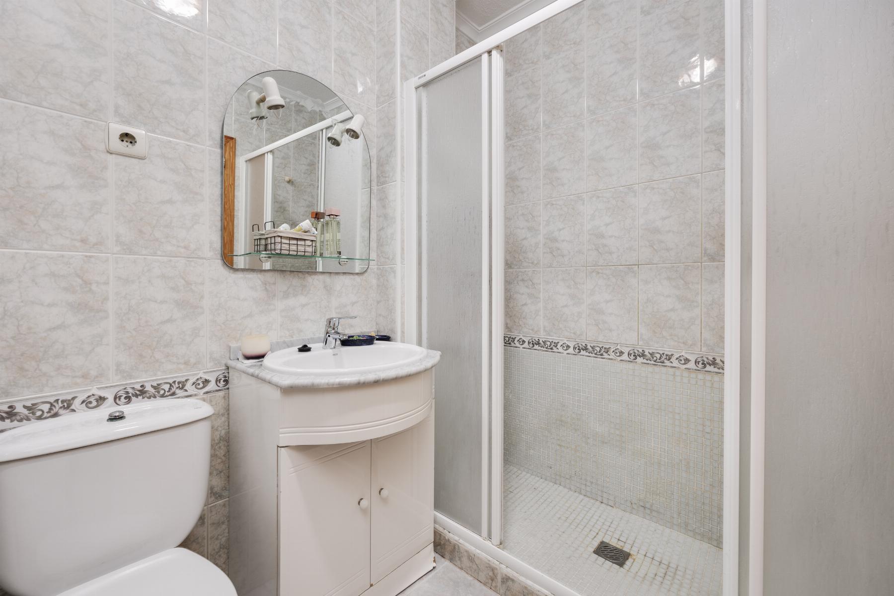 Small bathroom with a white vanity sink, oval mirror, and a glass‑door shower against tiled walls.