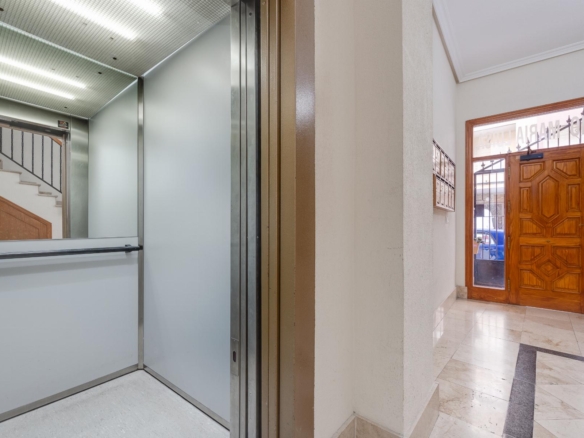 Open elevator doors in a building lobby, with a marble floor and wooden entrance door outside visible to the right.