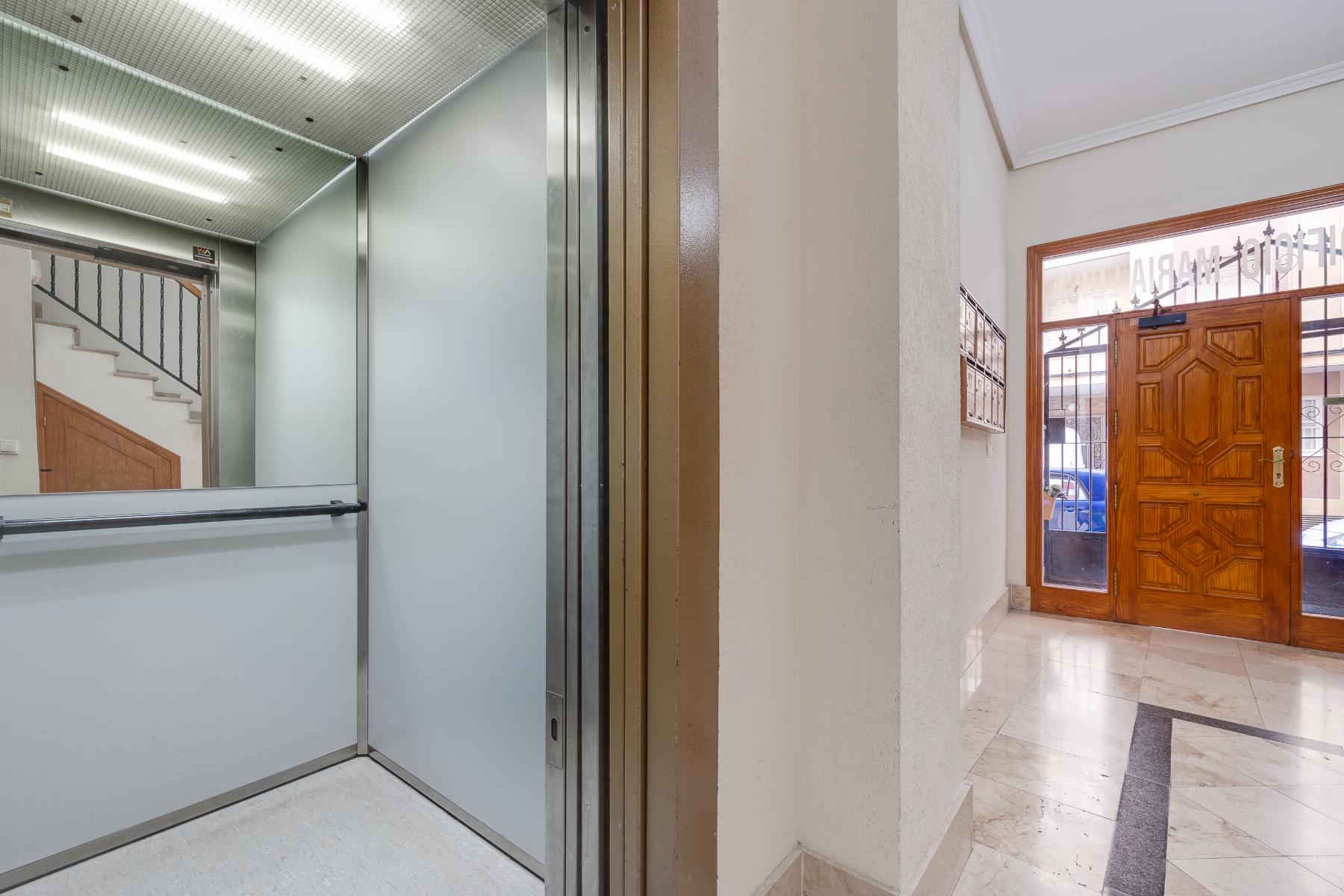 Open elevator doors in a building lobby, with a marble floor and wooden entrance door outside visible to the right.