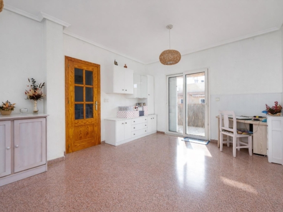 Bright, minimalist room with white cabinets, a wooden door, and a glass patio door letting in light; a desk and chair on the right.