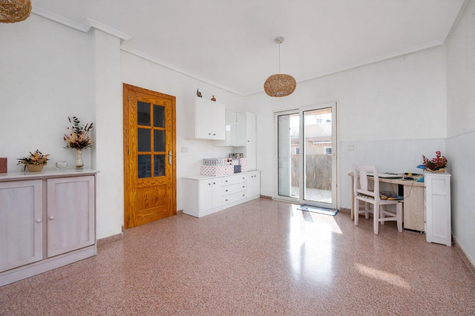 Bright, minimalist room with white cabinets, a wooden door, and a glass patio door letting in light; a desk and chair on the right.