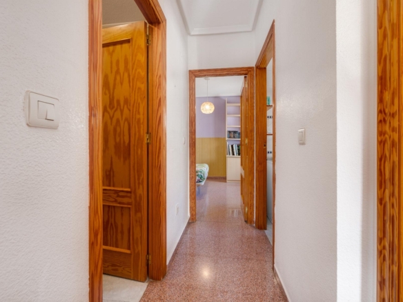 Hallway with white walls and open wooden door frames, leading to a bedroom with a bed and bookshelf.