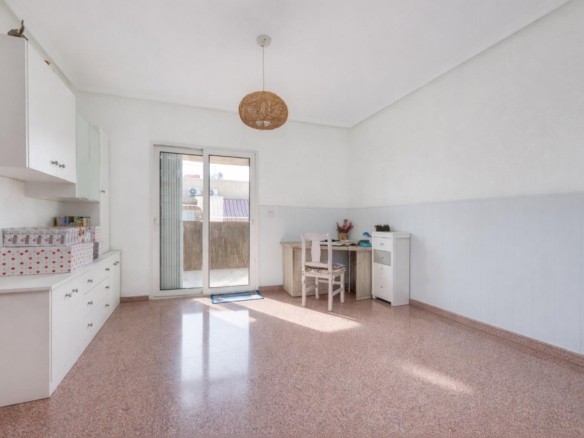 Bright room with white cabinets along the left wall, pink terrazzo floor, and a sliding door to an outdoor area, with a desk and chair on the right side.