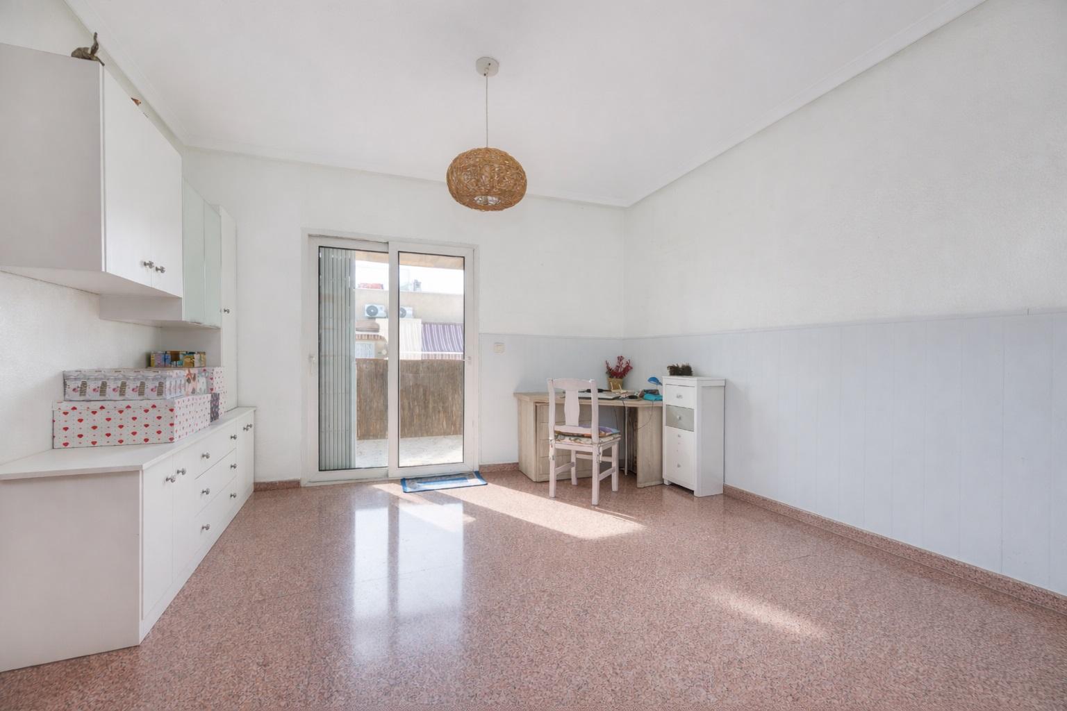 Bright room with white cabinets along the left wall, pink terrazzo floor, and a sliding door to an outdoor area, with a desk and chair on the right side.