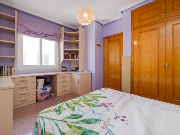 Bedroom with purple walls, built-in light wood desk and shelves, window, and large wooden wardrobes.