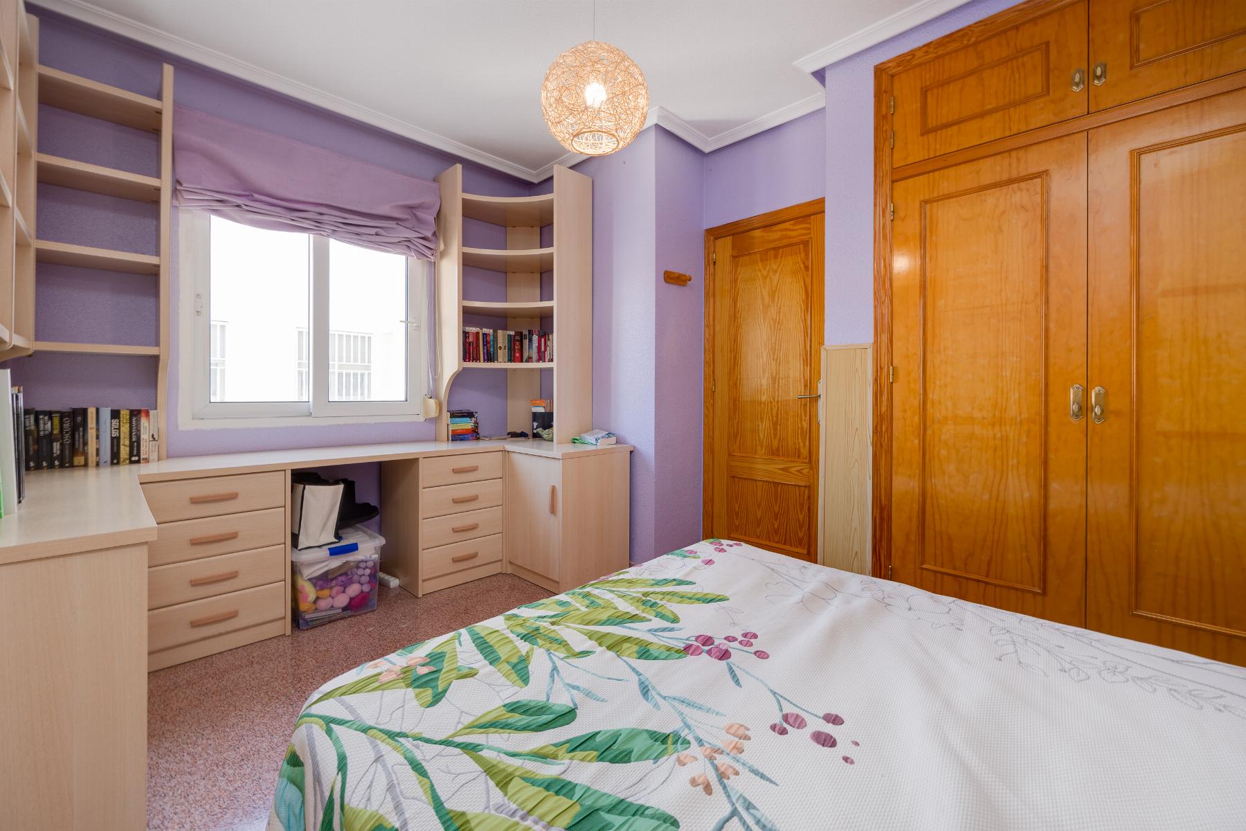 Bedroom with purple walls, built-in light wood desk and shelves, window, and large wooden wardrobes.