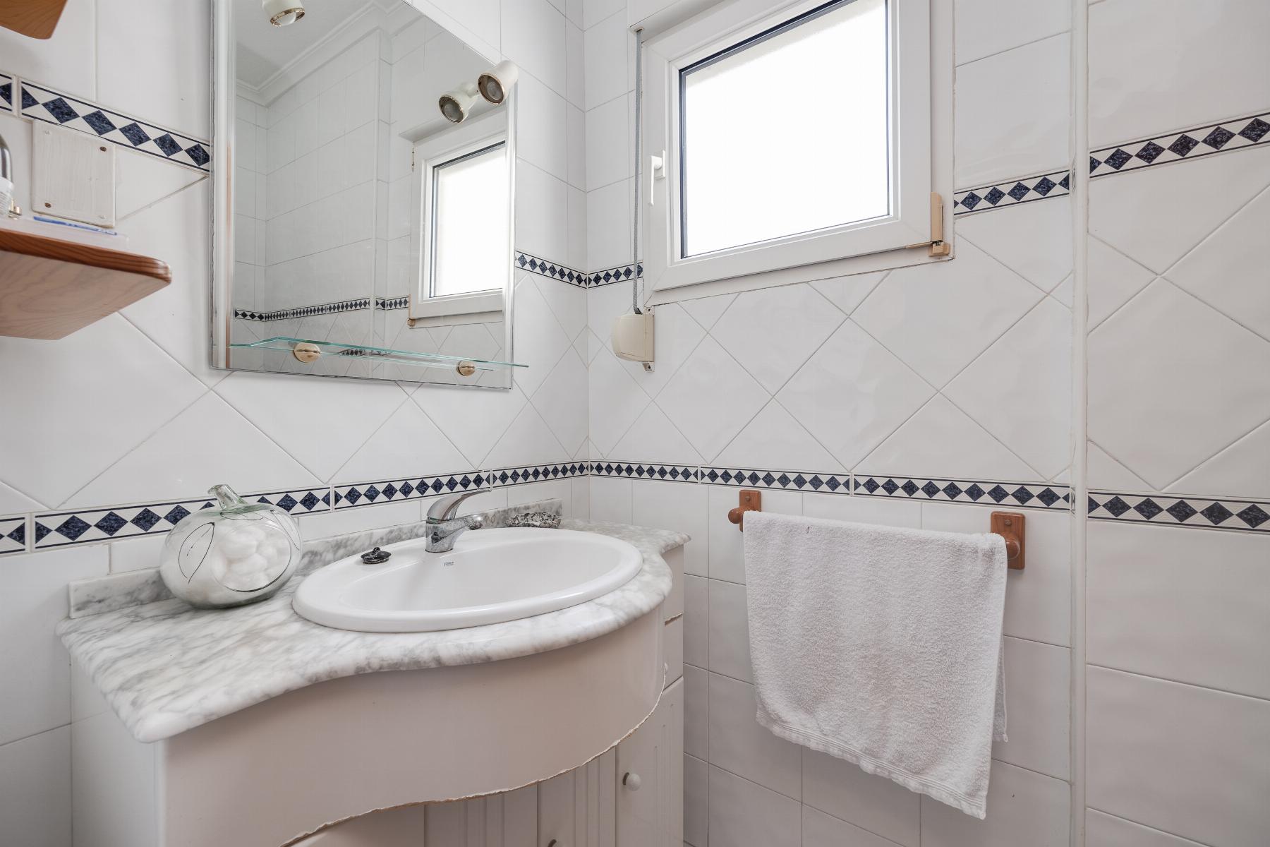 White tiled bathroom with a marble countertop sink, mirror, and a towel hanging on a rack near a window. The blue diamond tile border runs around the walls.