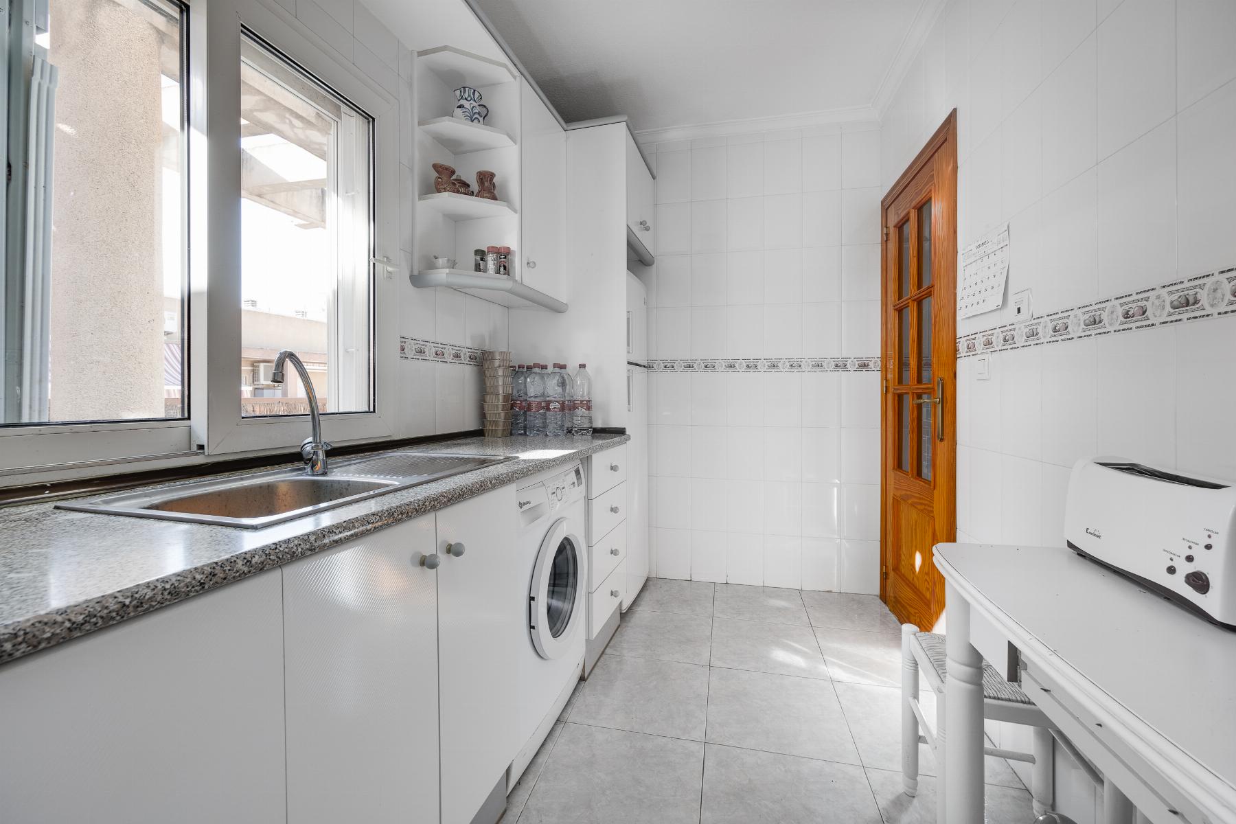 Bright white kitchen with a double sink by a large window and a row of white cabinets and a washing machine underneath the counter.