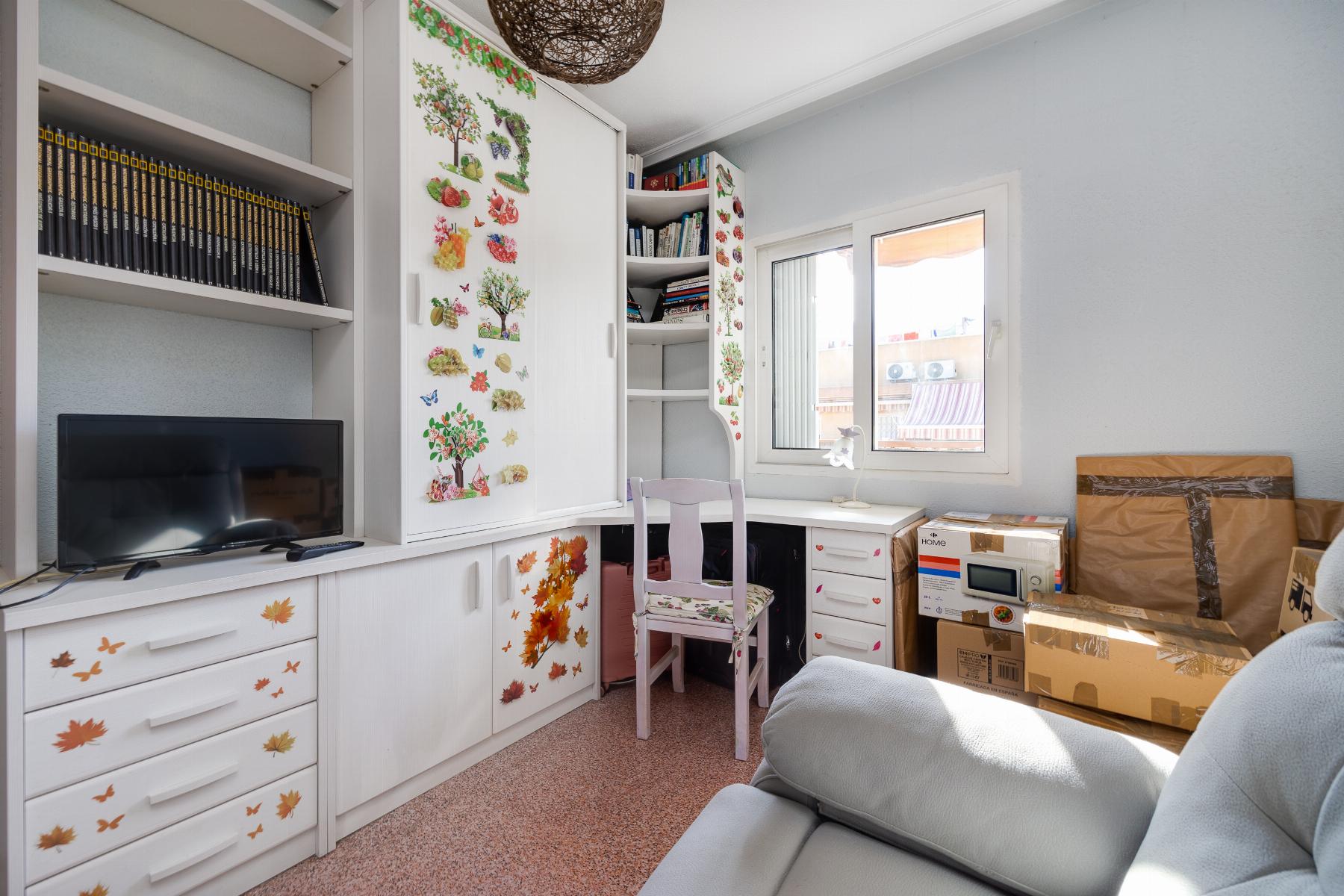 White built-in desk and cabinets decorated with autumn leaf stickers, a chair, bookshelves, a small TV, and a window in a bright room.
