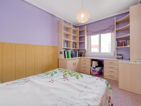Bedroom with lavender walls, built-in light wood shelves, and a bed with floral duvet near a window.