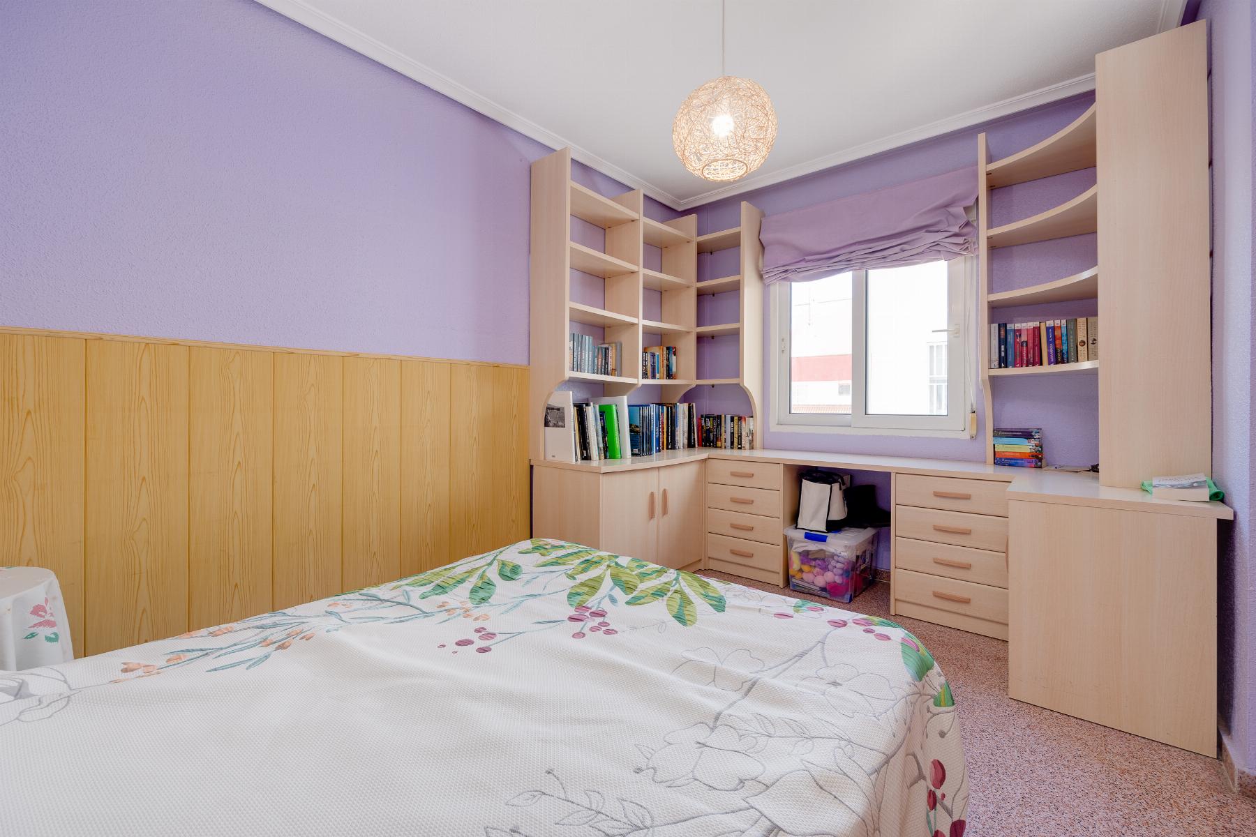 Bedroom with lavender walls, built-in light wood shelves, and a bed with floral duvet near a window.