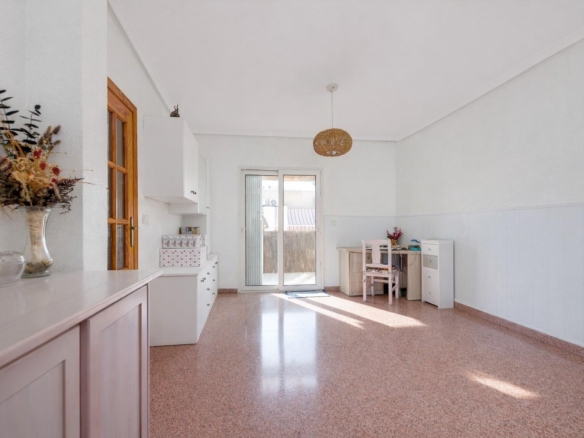 Sunlit, minimalist room with white walls, pale furniture along the left wall, and a glass patio door at center.