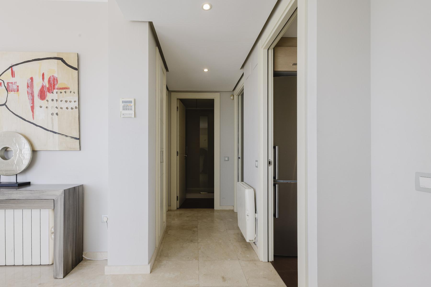 Bright, modern hallway with light gray walls, abstract painting on the left, and doors at the far end.