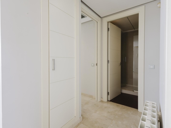 Narrow hallway with white built‑in wardrobes on the left and a bathroom door open to a tiled shower area