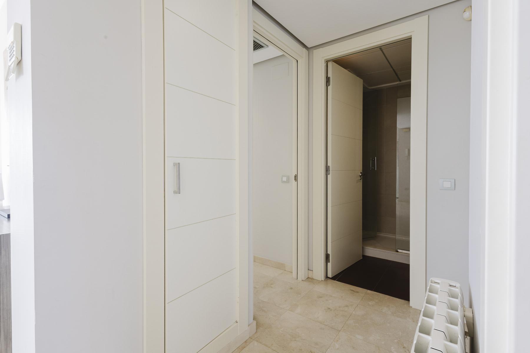 Narrow hallway with white built‑in wardrobes on the left and a bathroom door open to a tiled shower area