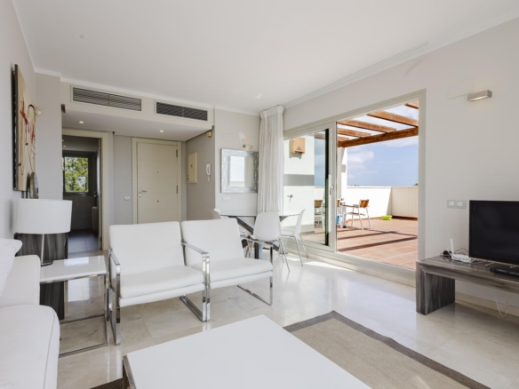 Bright modern living room with white seating and a sliding glass door opening to a sunny terrace outside.