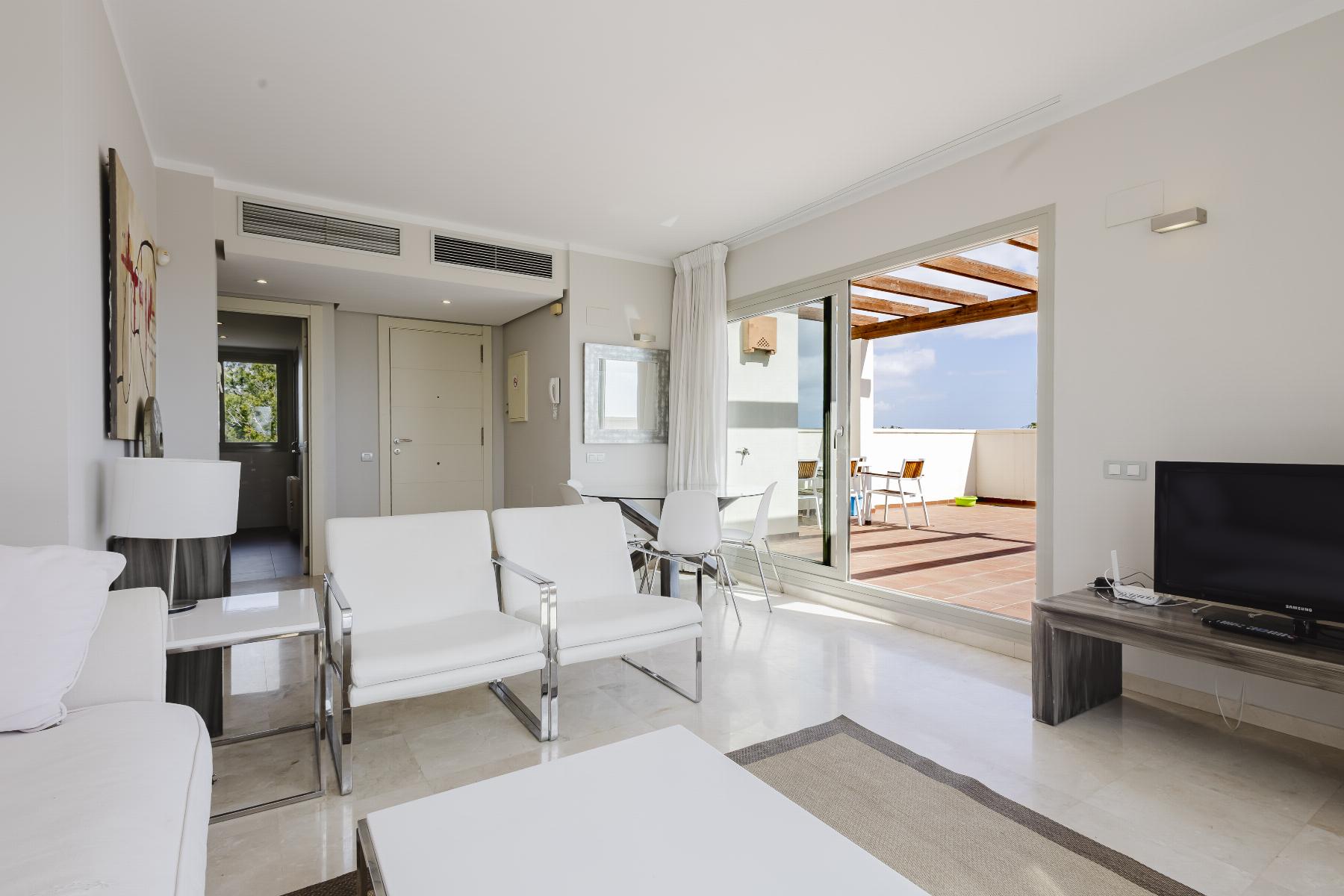 Bright modern living room with white seating and a sliding glass door opening to a sunny terrace outside.