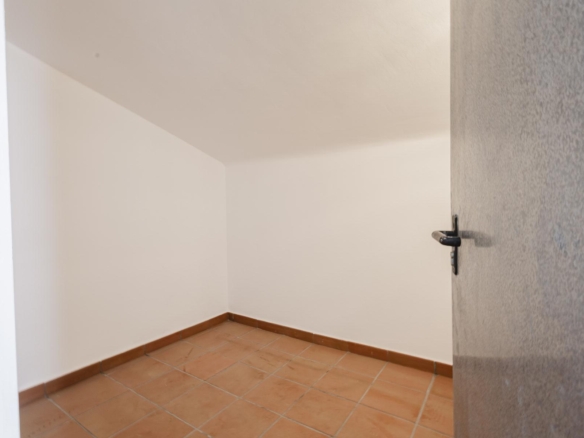 Small empty room with white walls, terracotta tile floor, and a partially open gray door visible on the right side.