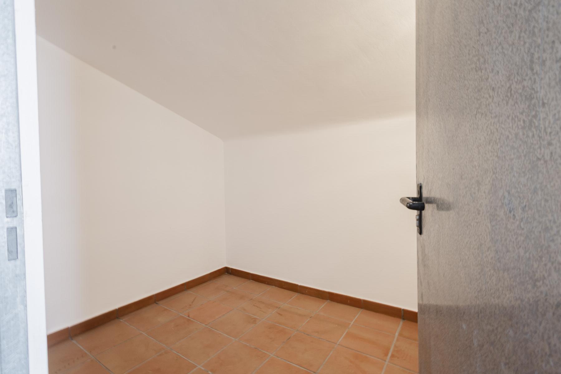 Small empty room with white walls, terracotta tile floor, and a partially open gray door visible on the right side.