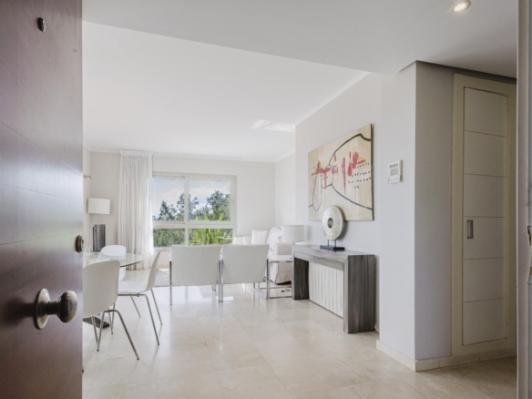 Bright, modern dining and living area with white chairs around a glass table, large window, and neutral decor.