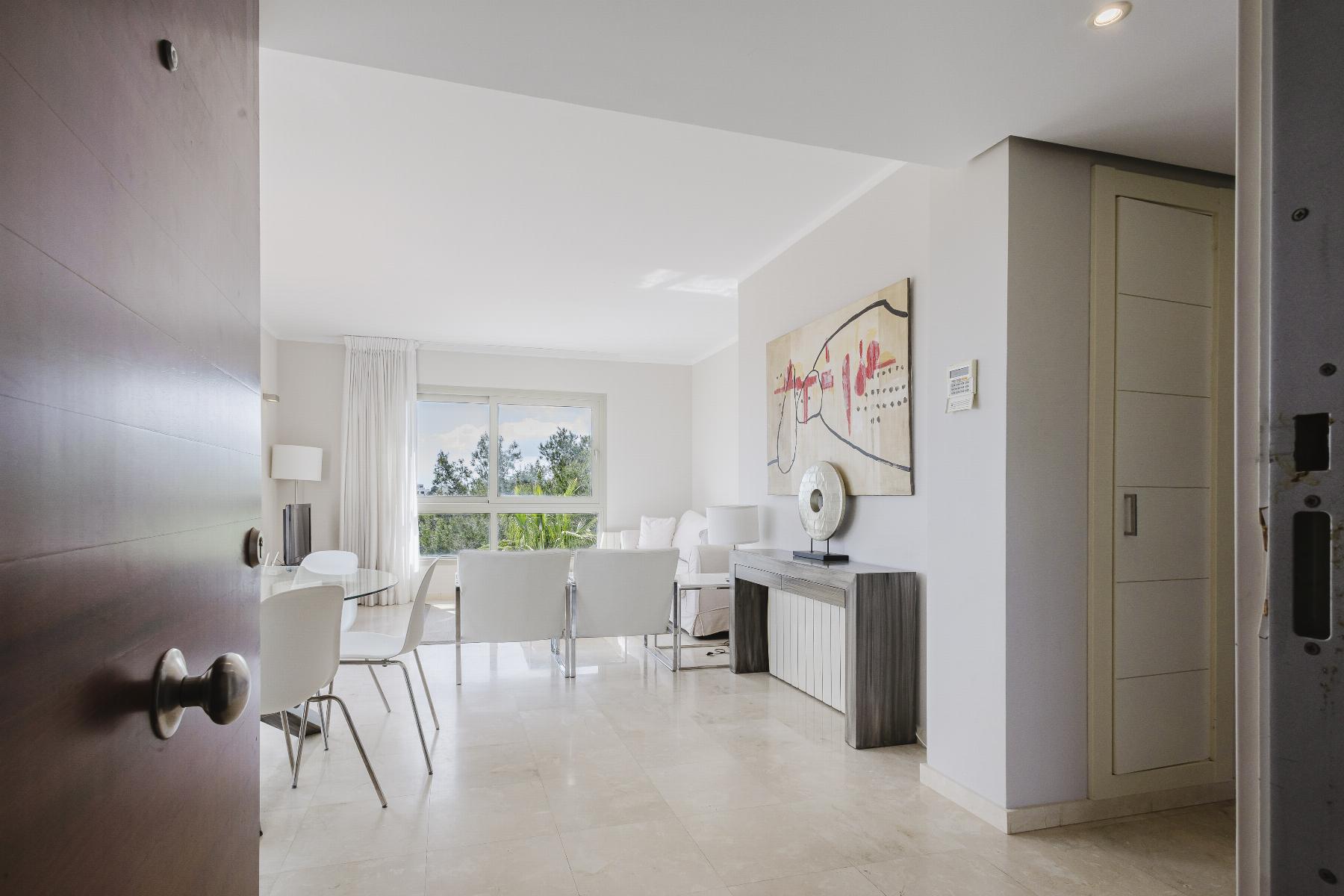 Bright, modern dining and living area with white chairs around a glass table, large window, and neutral decor.