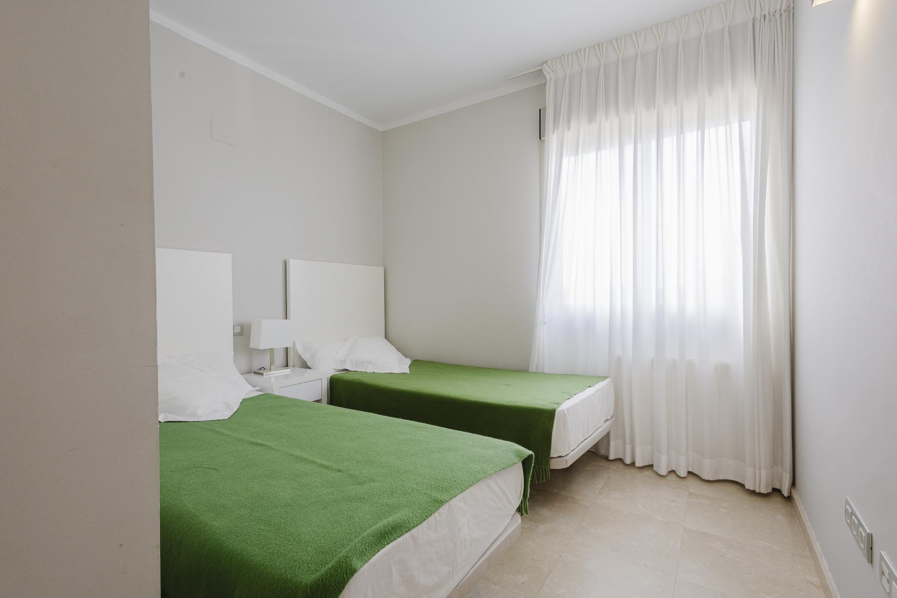 Twin hotel room with two single beds in green bedspreads and white headboards beside a nightstand and lamp under soft natural light.