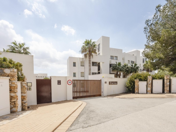 Gated white residential complex with palm trees and stone walls under a blue sky.