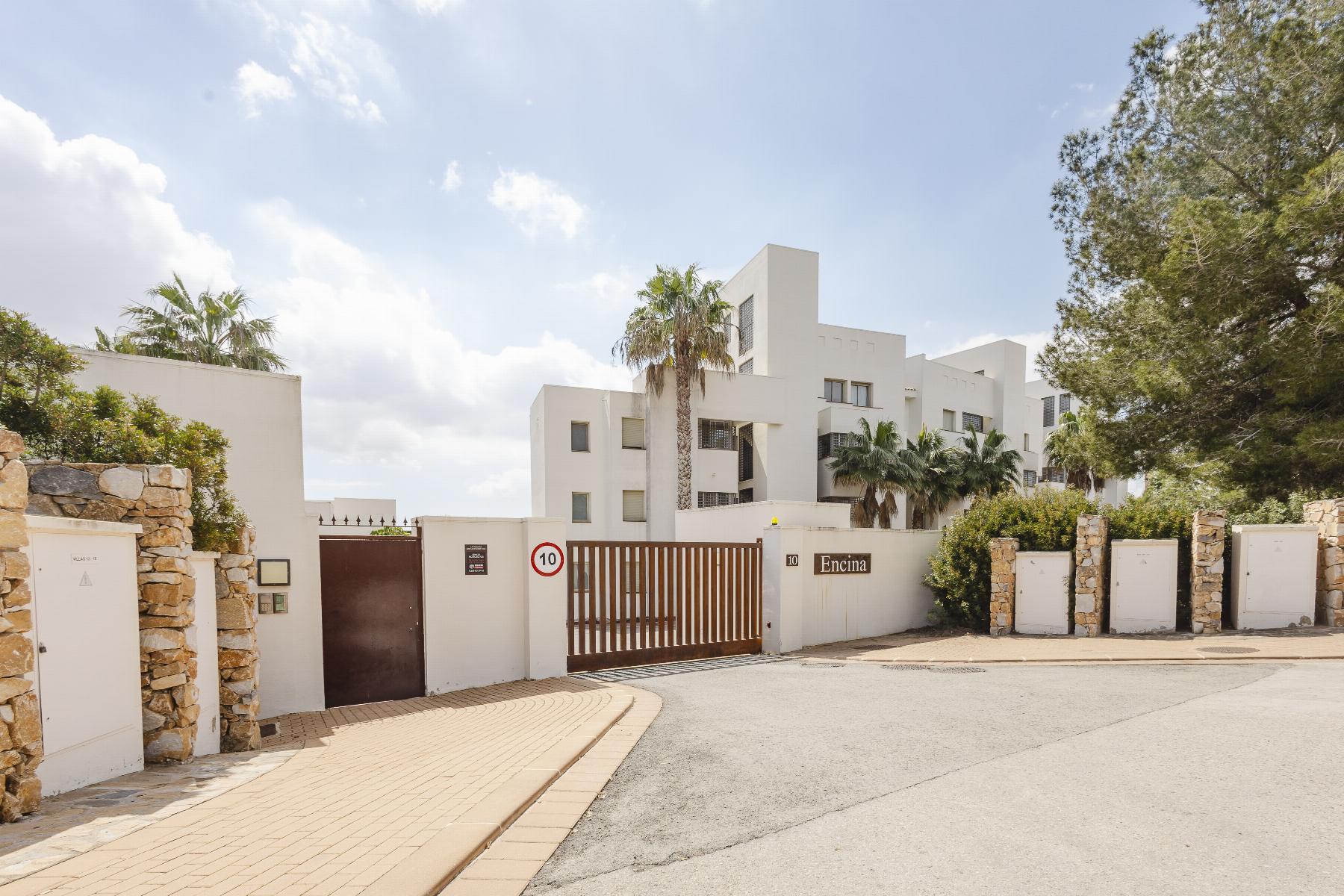 Gated white residential complex with palm trees and stone walls under a blue sky.
