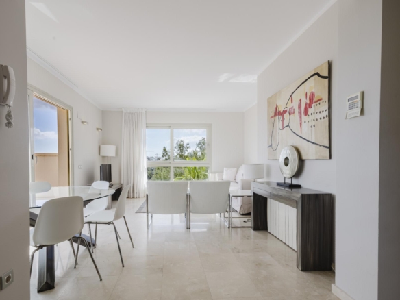 Bright modern living and dining area with a glass dining table, white chairs, and a large abstract painting on the wall.