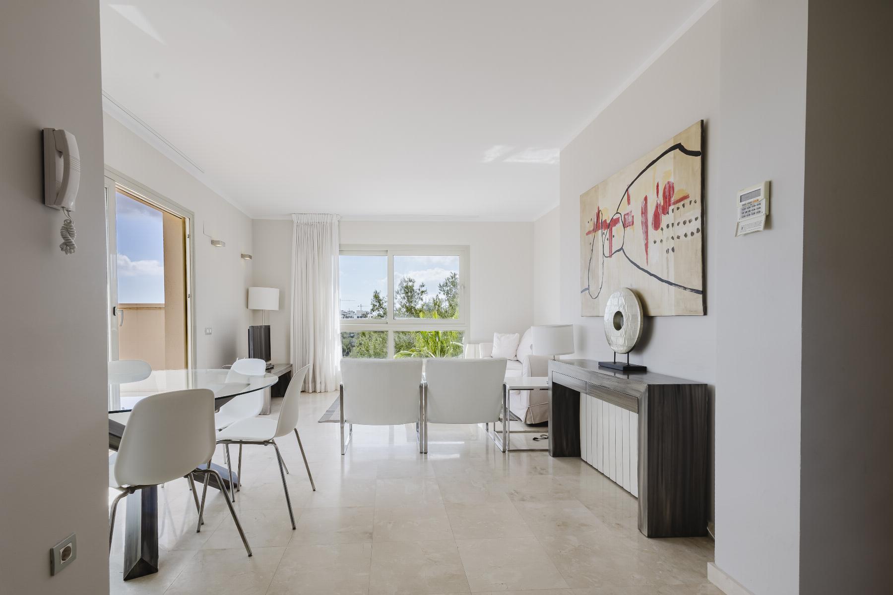 Bright modern living and dining area with a glass dining table, white chairs, and a large abstract painting on the wall.