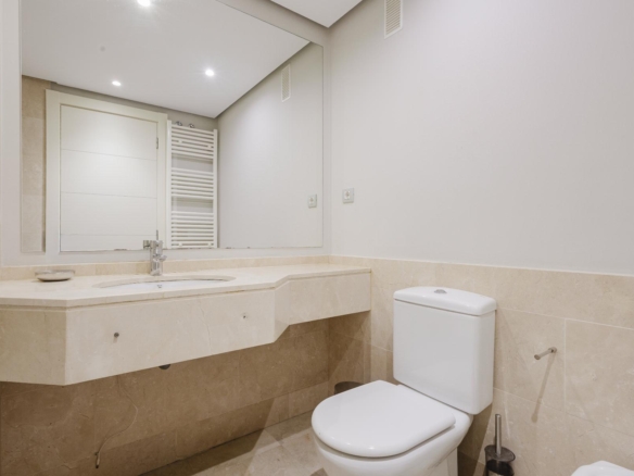 Modern beige-tiled bathroom with a wall-mounted sink, large mirror, and white toilet.