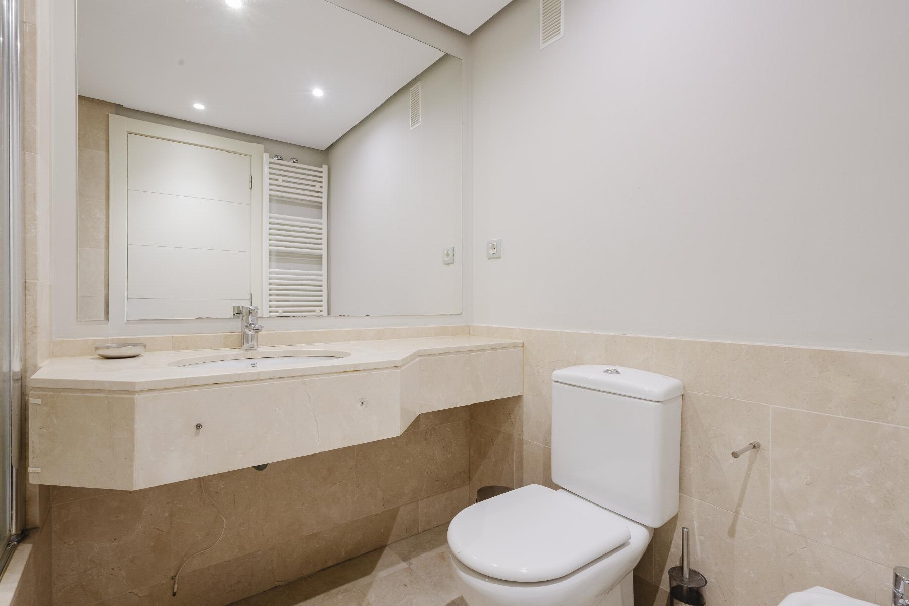 Modern beige-tiled bathroom with a wall-mounted sink, large mirror, and white toilet.