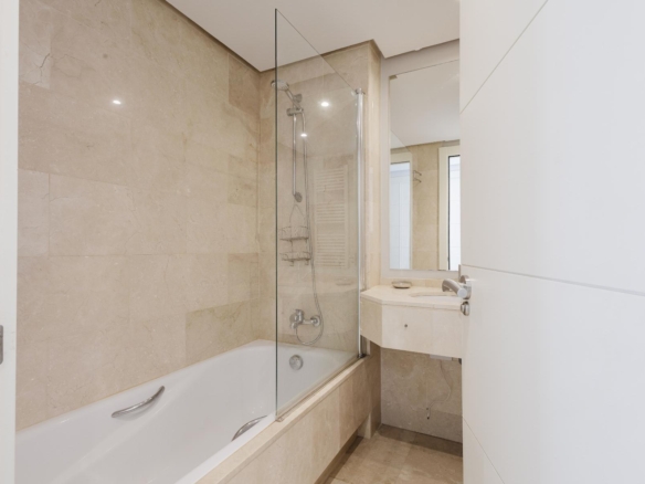 Modern beige-tiled bathroom with a glass shower enclosure, bathtub, and a white sink with mirror.