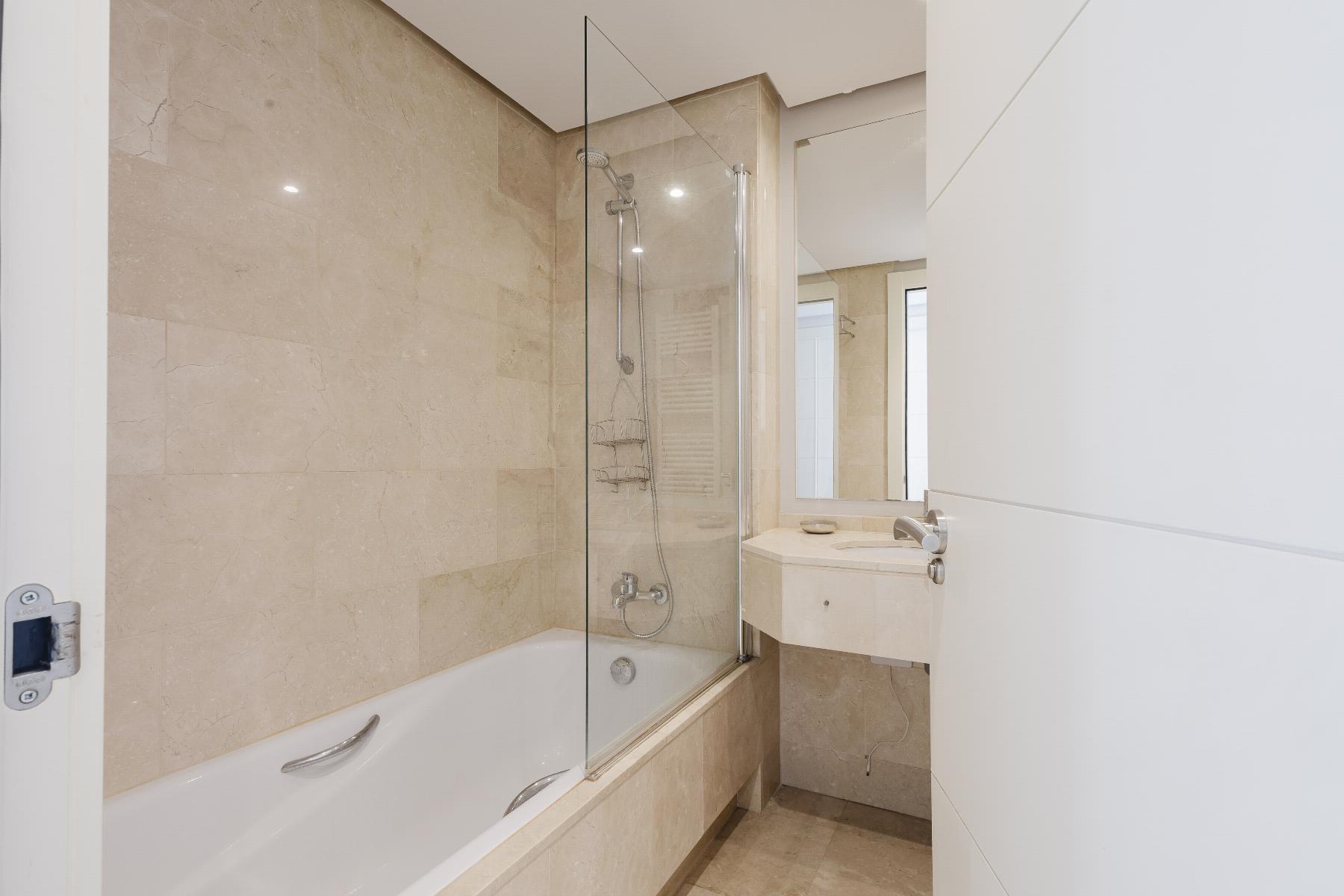 Modern beige-tiled bathroom with a glass shower enclosure, bathtub, and a white sink with mirror.