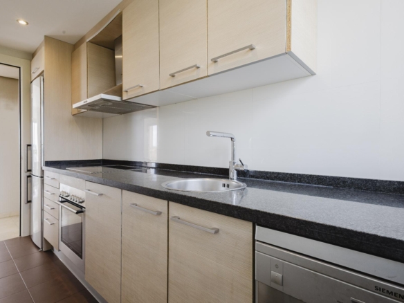 Modern kitchen with light wood cabinets, black granite countertop, and stainless steel appliances including a sink and range hood