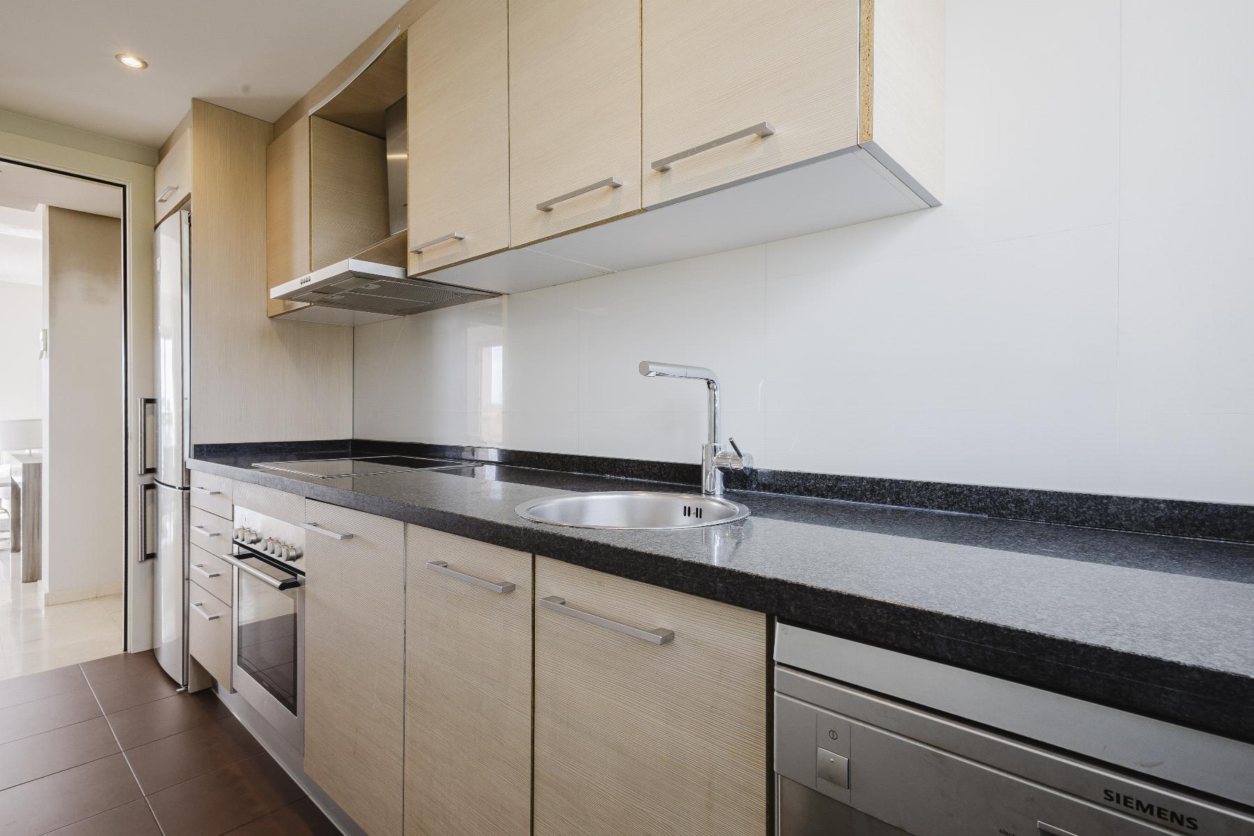 Modern kitchen with light wood cabinets, black granite countertop, and stainless steel appliances including a sink and range hood