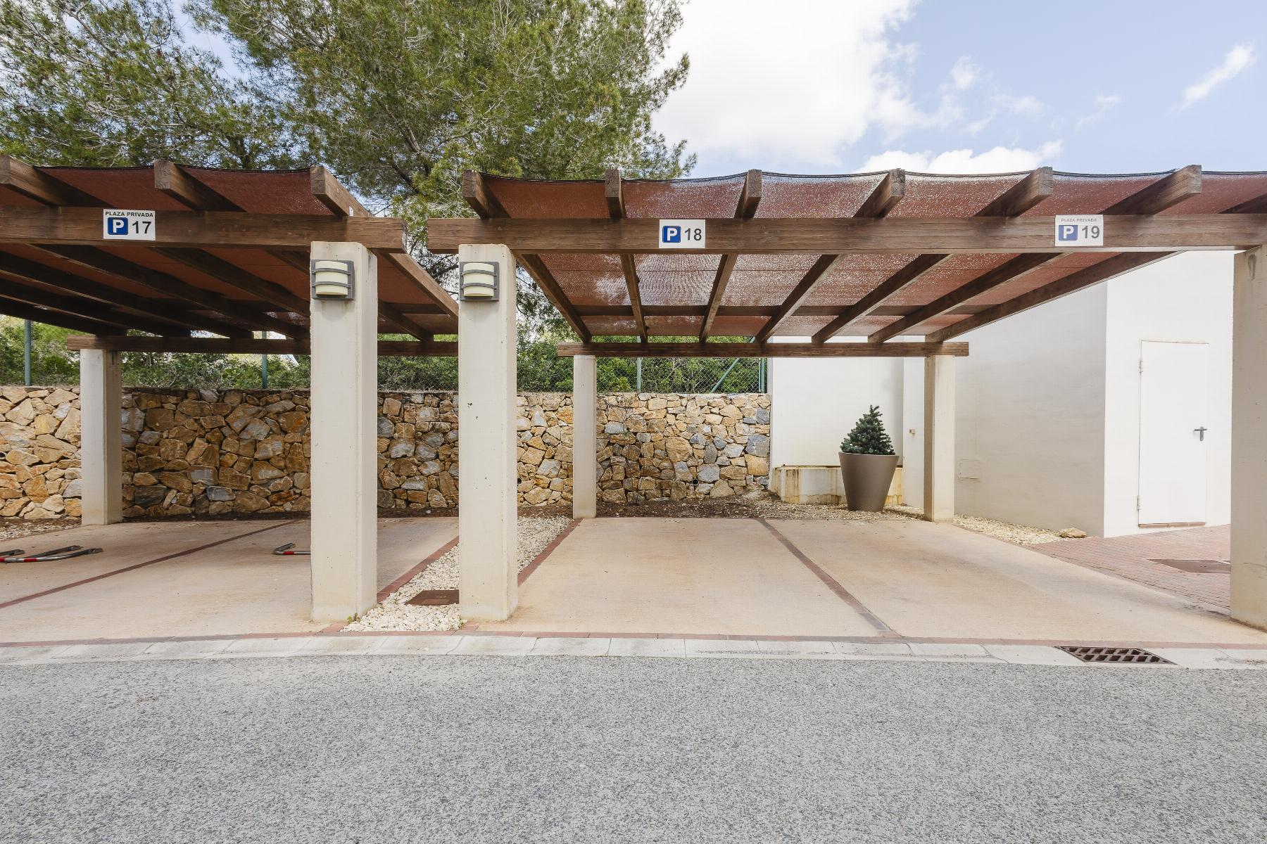 A covered parking area with wooden beams, concrete columns, and a stone wall in the background, labeled spots P17–P19 with a potted plant near a white wall and door on the right
