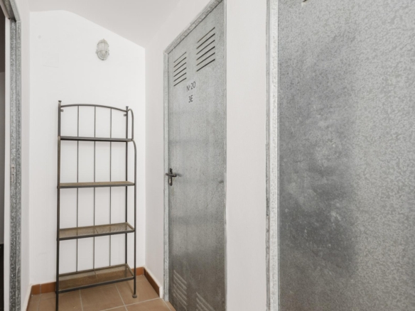 Narrow utility space with a tall metal shelving unit beside a gray metal locker labeled No. 20 3E in a white-walled room.