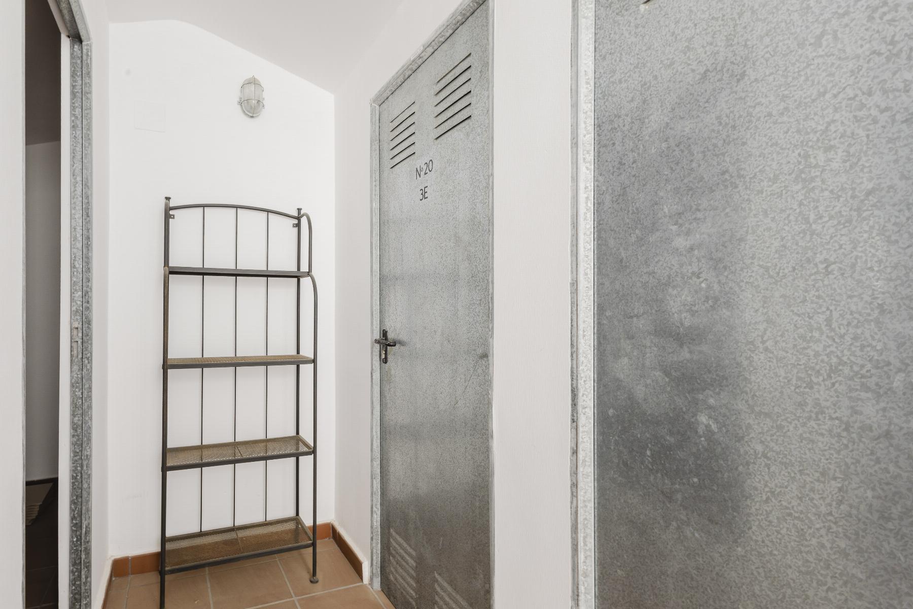 Narrow utility space with a tall metal shelving unit beside a gray metal locker labeled No. 20 3E in a white-walled room.