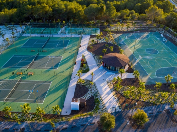 Aerial view of a recreational complex with multiple fenced tennis courts on the left and a large multiuse court on the right, surrounded by trees and a central gazebo.
