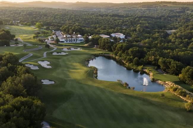 Aerial view of a lush golf course with sand traps, a winding fairway, and a central pond near a clubhouse surrounded by trees.