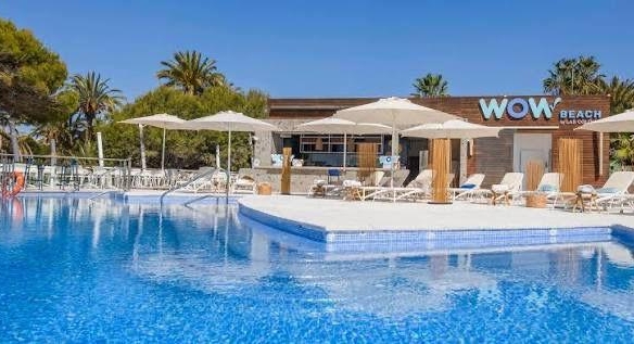Outdoor resort pool with blue water, white lounge chairs, and palm trees; building labeled 'WOW Beach' in background.